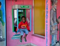 A child sits in a phone box outside Moses Mabhida Library in Khayelitsha. Photo by Kate Stegeman.