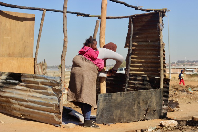 Photo of a woman with a baby on her back erecting a shack