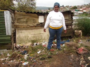 Photo of woman and pile of rubbish in front of her shack
