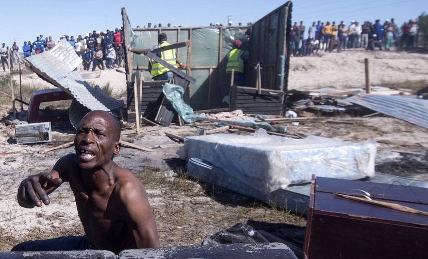 Alex Midikana sits amongst his belongings as shacks are removed. When Law Enforcement arrived yesterday, Midikana’s home was spared. Today it too was removed. Photo: Brenton Geach