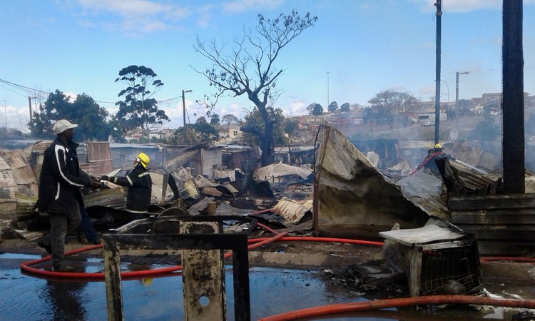 Photo of firefighters and burnt shacks