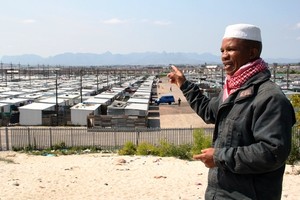 Photo of a man pointing to rows of zinc houses