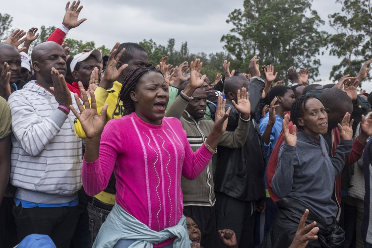 People raise their hands in prayer at the Zimbabwe Grounds.