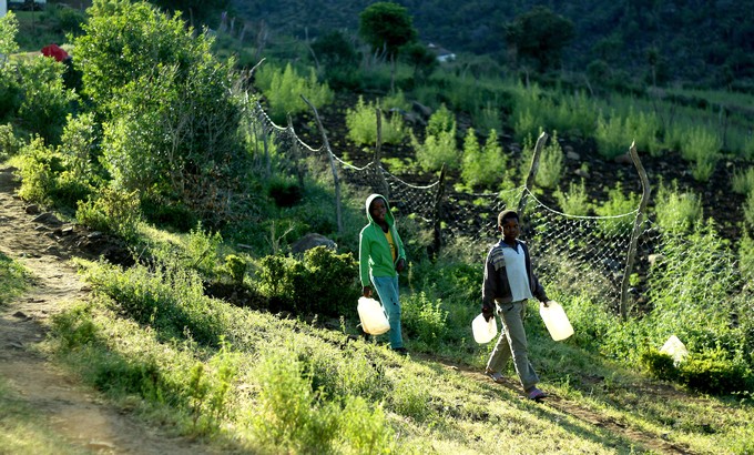 Ongezile (green jacket) and Siya walk down the hill with empty buckets.