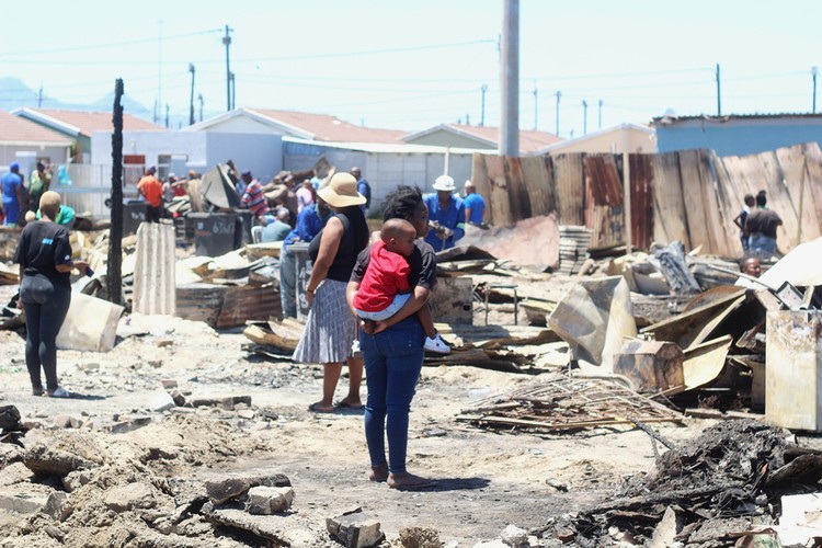 A woman with a young child stands among the charred remains after a fire destroyed 81 shacks on Saturday morning in Khayelitsha. Photo: Masixole Feni