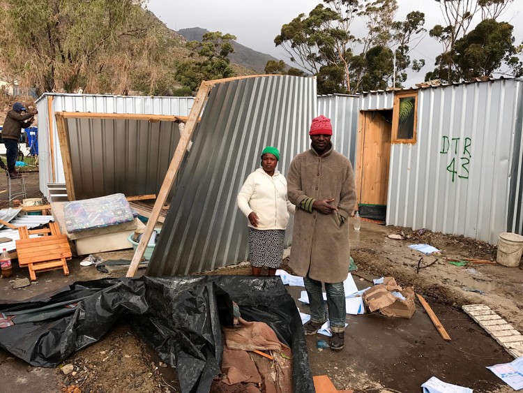 Photo of two people in front of blown-down shack