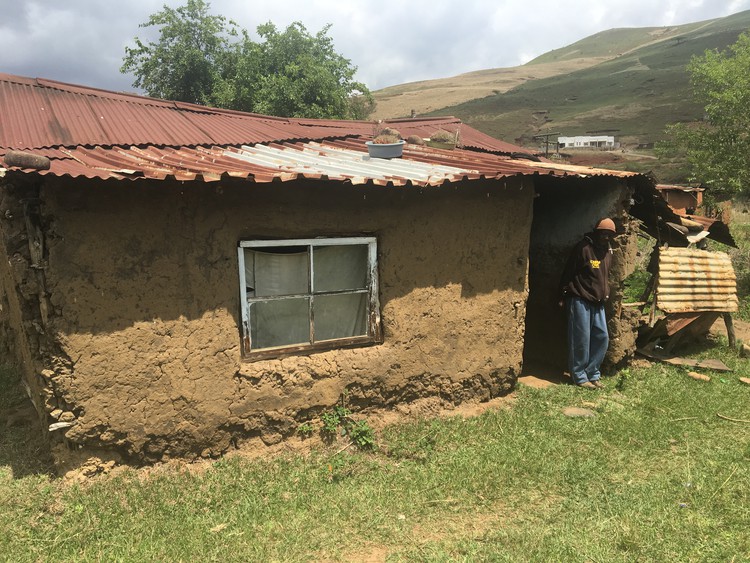 Photo of man in front of mud house