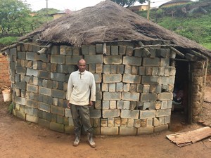 Photo of man in front of his hut