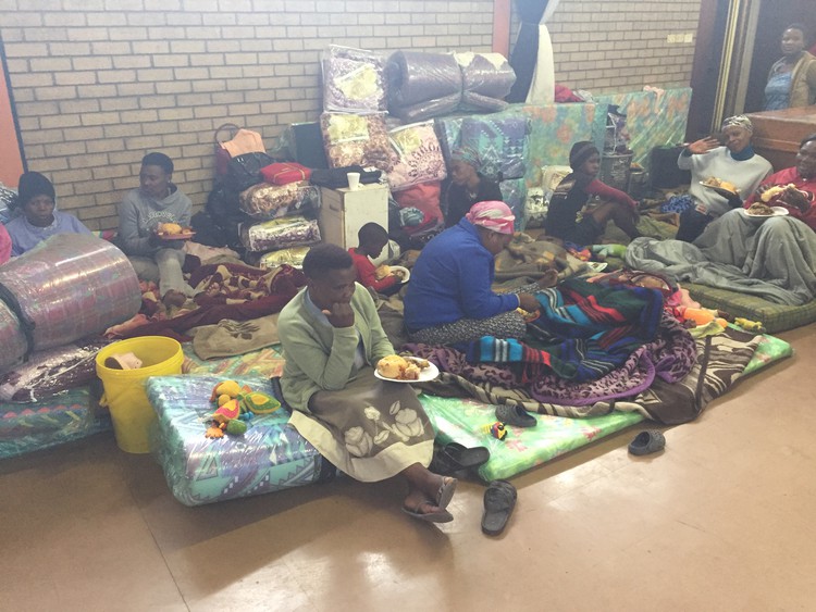 Photo of resdents sitting with their belongings in the community hall
