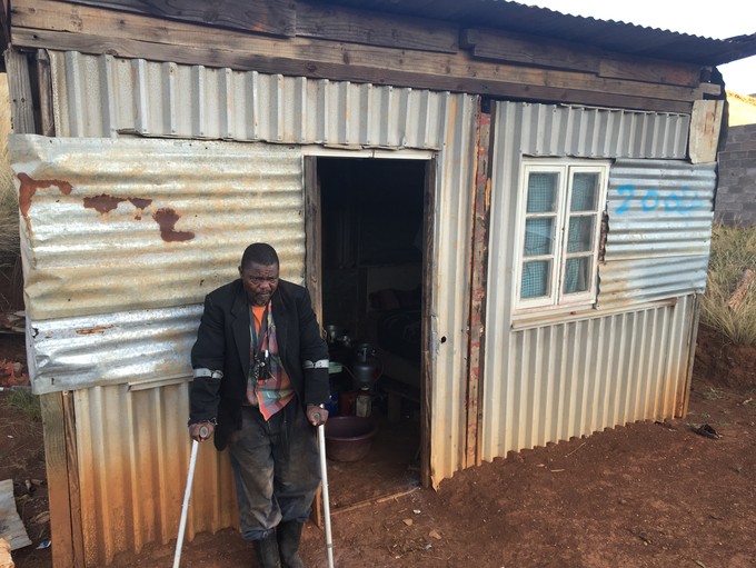 Photo of man with crutches in front of his shack