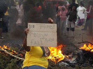 Photo of protester with placard saying Thandi Ndlovu must fall, in front of burning materials