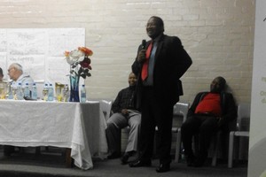 Photo of Advocate Vusi Pikoli speaking with a man sleeping behind him