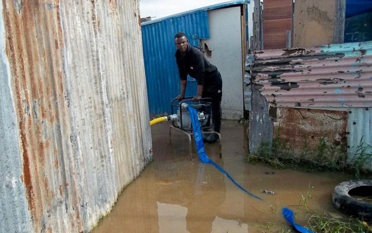 Photo of water being pumped from flooded shacks