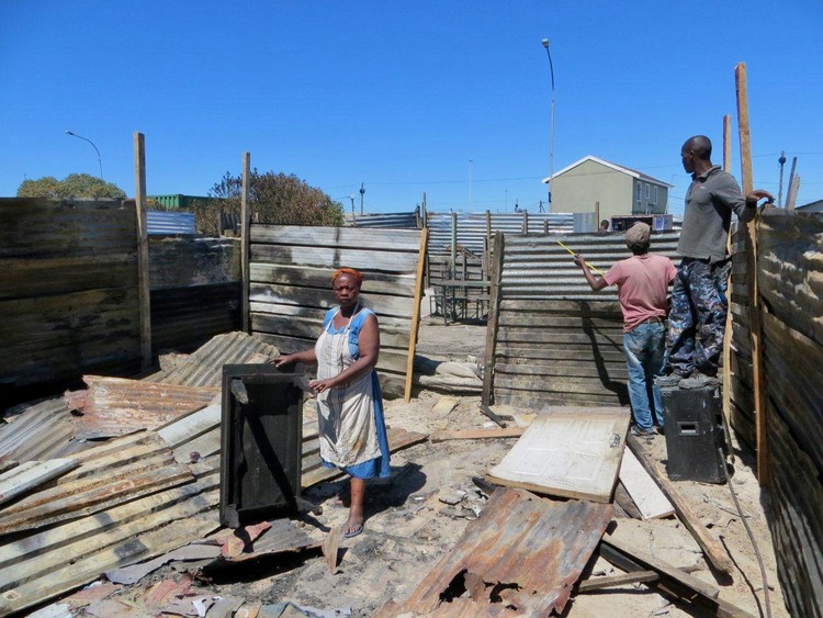 Khaziwe Dyantyi stands in the centre of her burnt shack while her brothers rebuild with charred material she was able to salvage from the blaze. She lost everything she owned in the fire. Photo: Vincent Lali